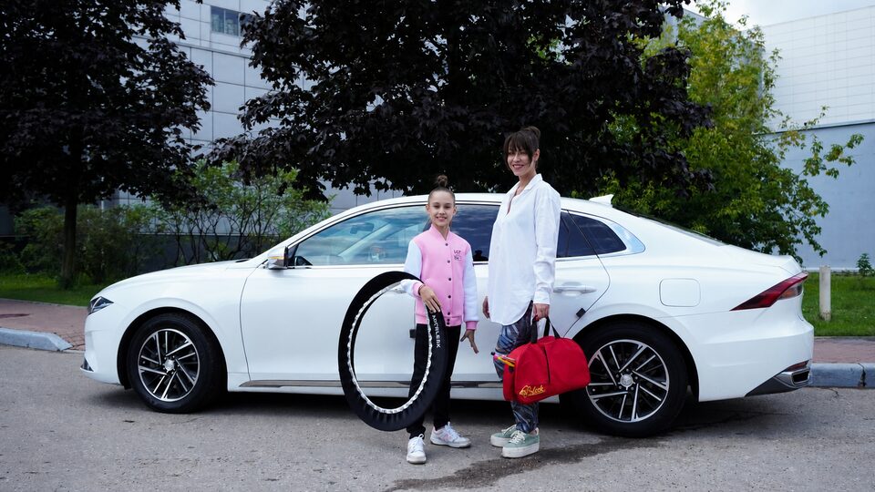 Автоняня и девочка с гимнастическим обручем у белого автомобиля