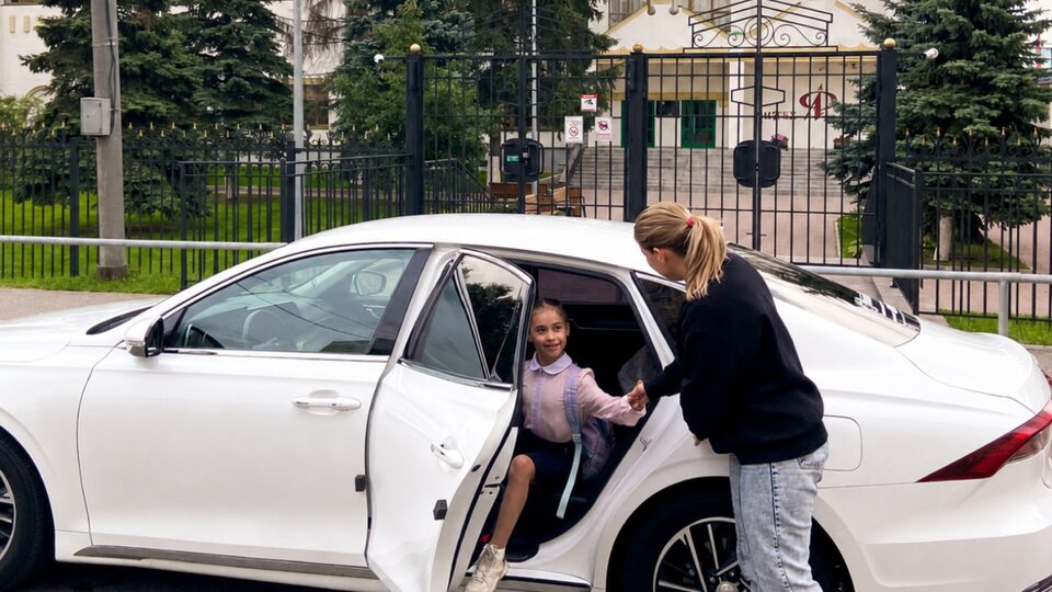 Автоняня подаёт руку школьнице, выходящей из машины у ворот
